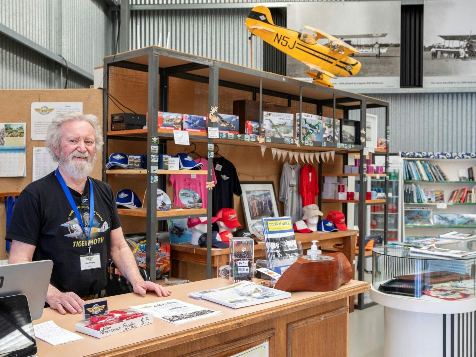 Man standing at a desk with a shelf of merchandise behind him