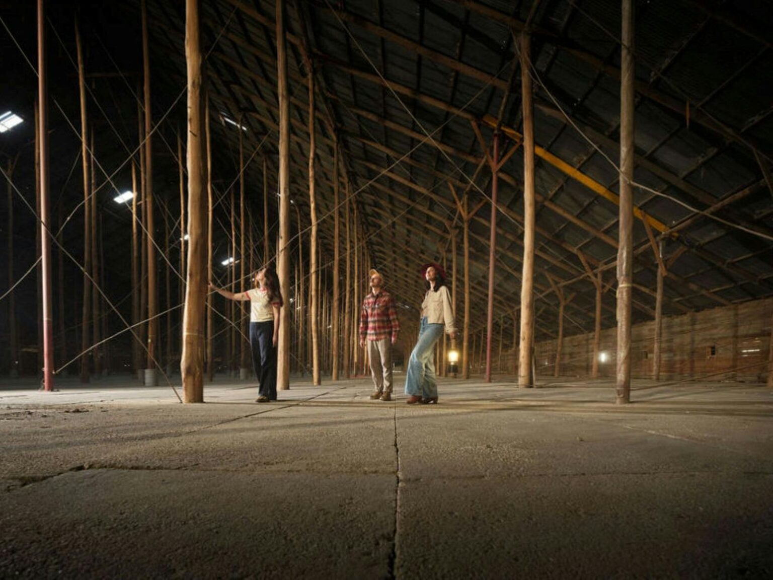 three people standing in a large shed surrounded by huge pillars and looking up