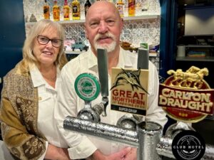 Two people standing behind the bar in a pub with beer taps in front of them
