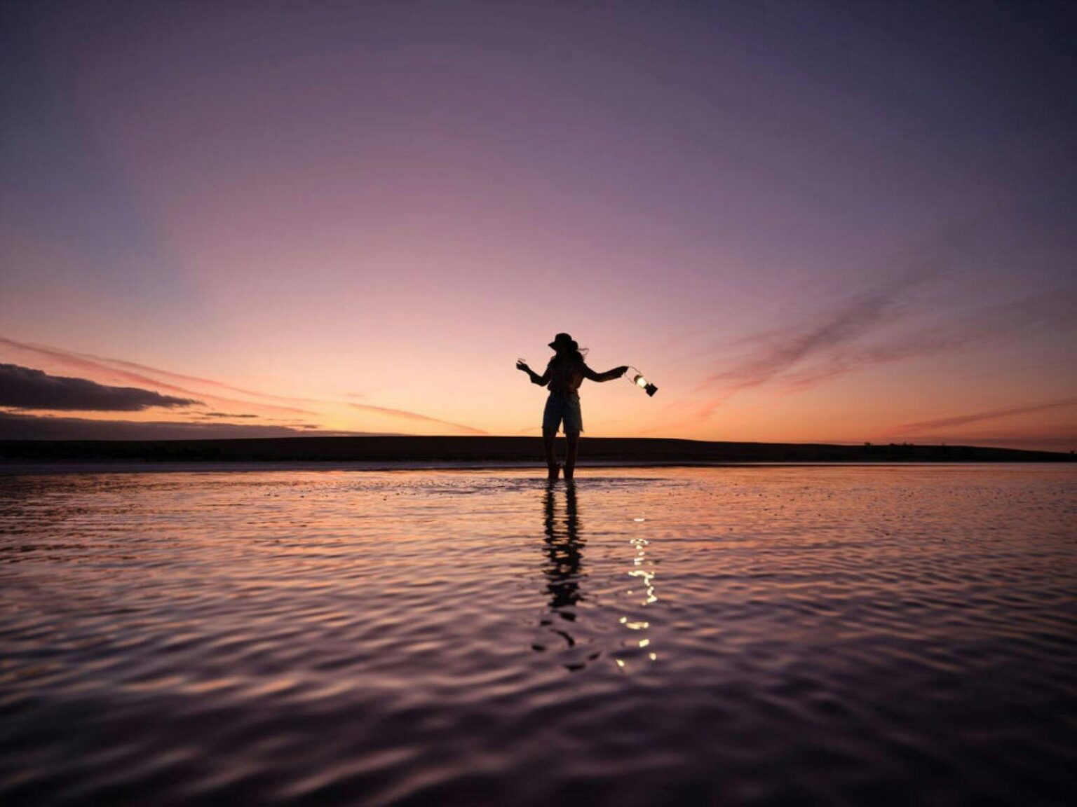A person standing on a salt lake as the sun sets