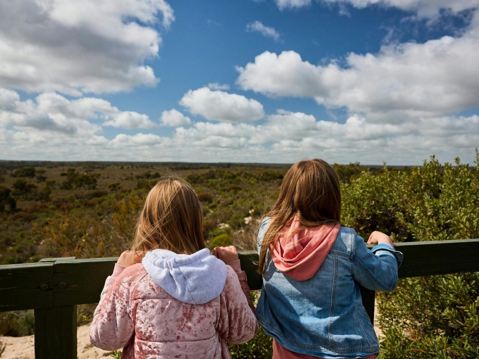 Two girls looking out over a lookout fence across scrubby desert landscape