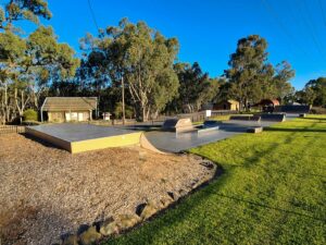 Skatepark with lawn surrounding and larger trees in background