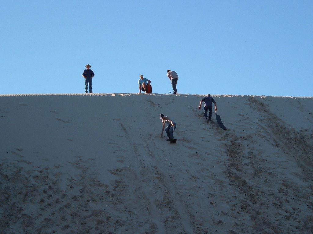 a group of people walking to the top of a large sand dune to discover what is at the top.