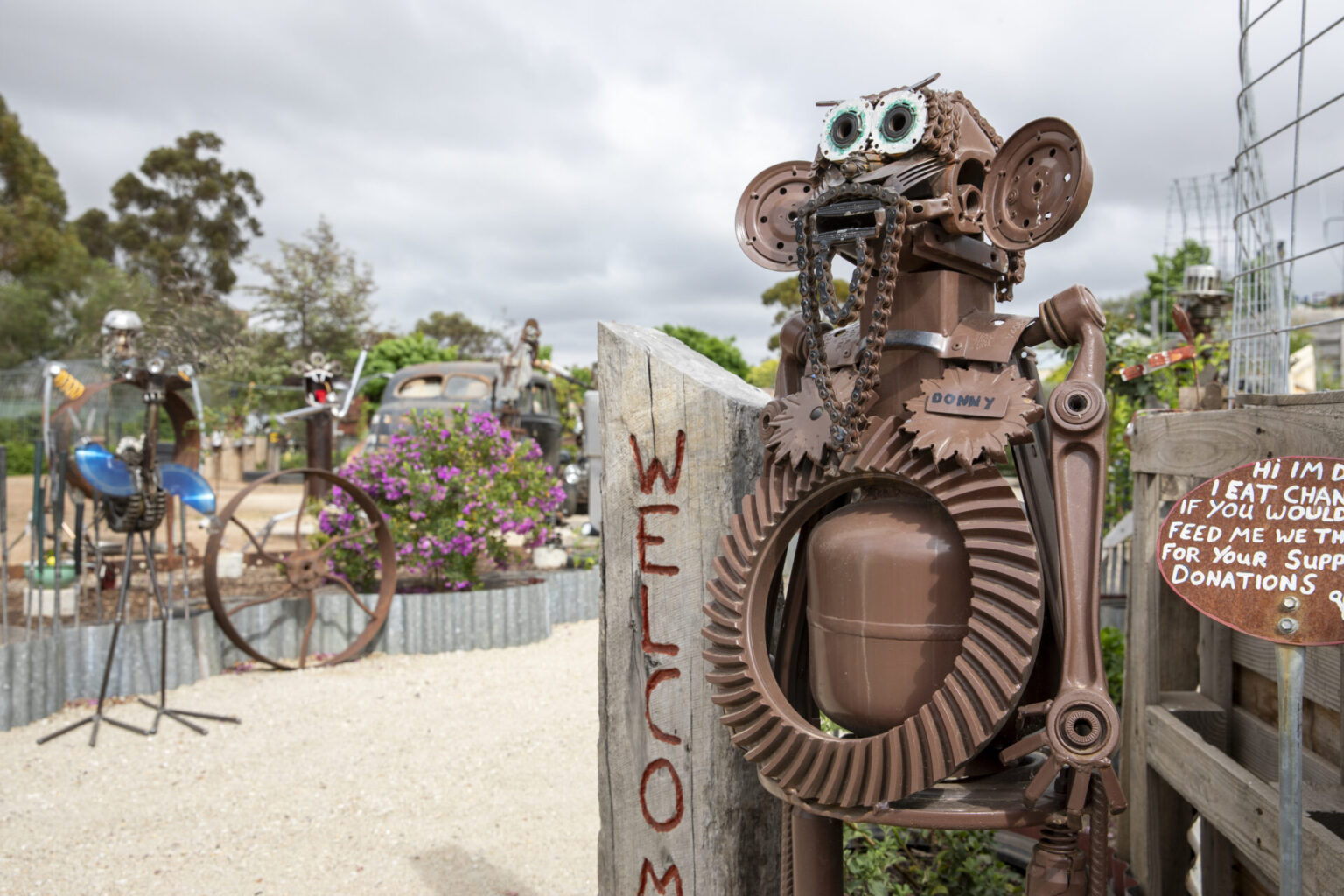 A large metal sculpture holding a welcome sign in front of an open garden area.