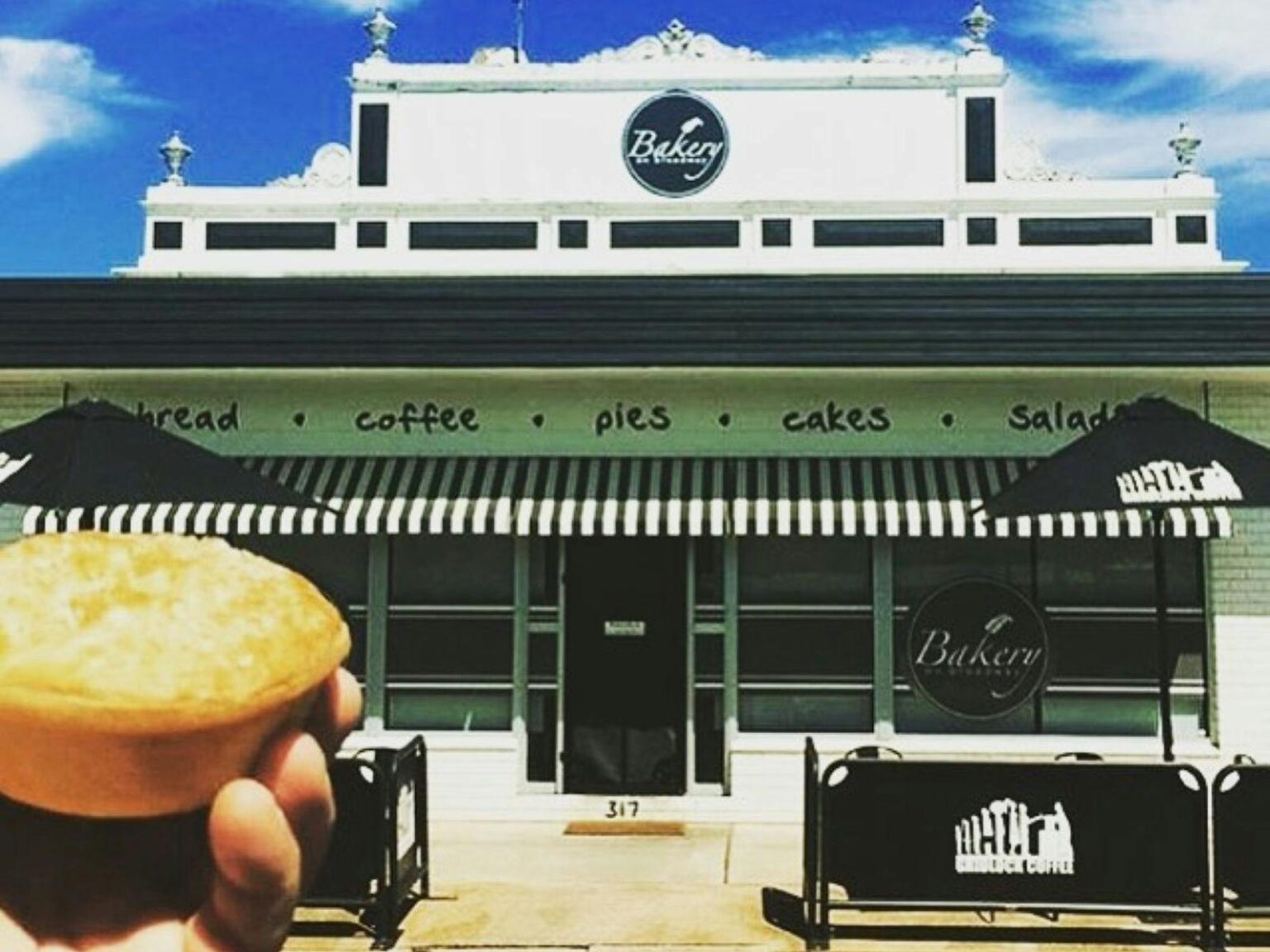 Exterior photo of a bakery with a hand holding up a pie