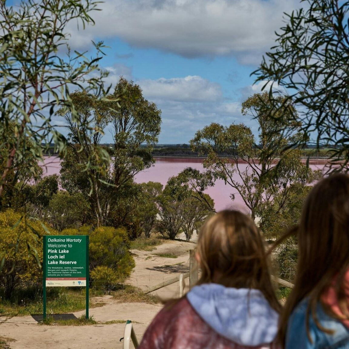 two girls looking down sandy walking track to pink lake