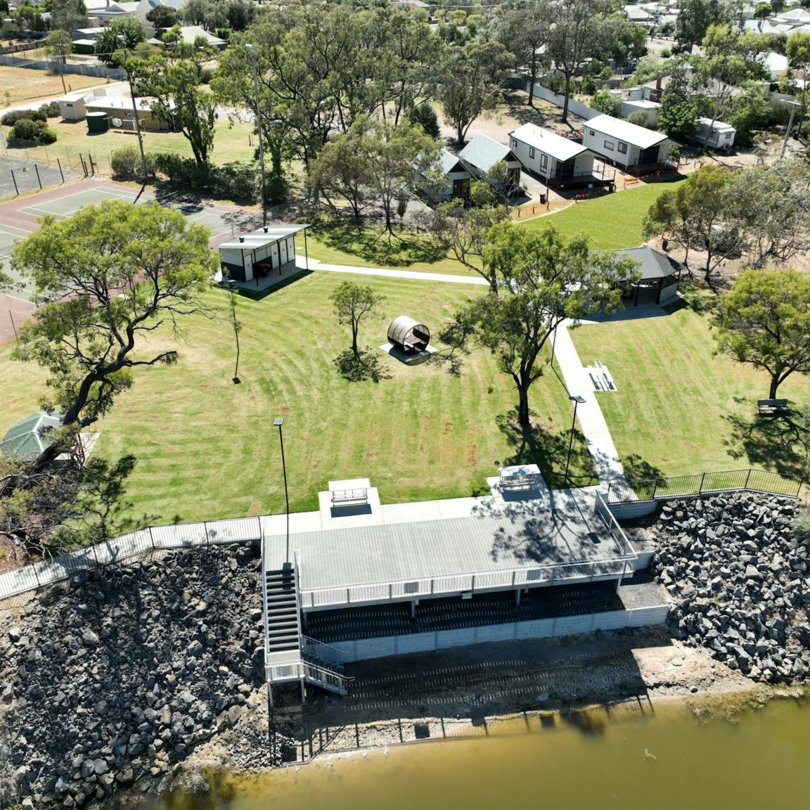 aerial view of river with grassed picnic area with cabins in background