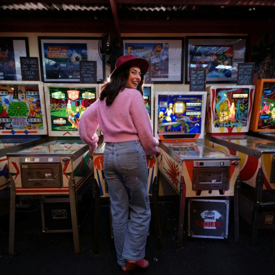 Person looking back over their shoulder and playing a row of pinball machines
