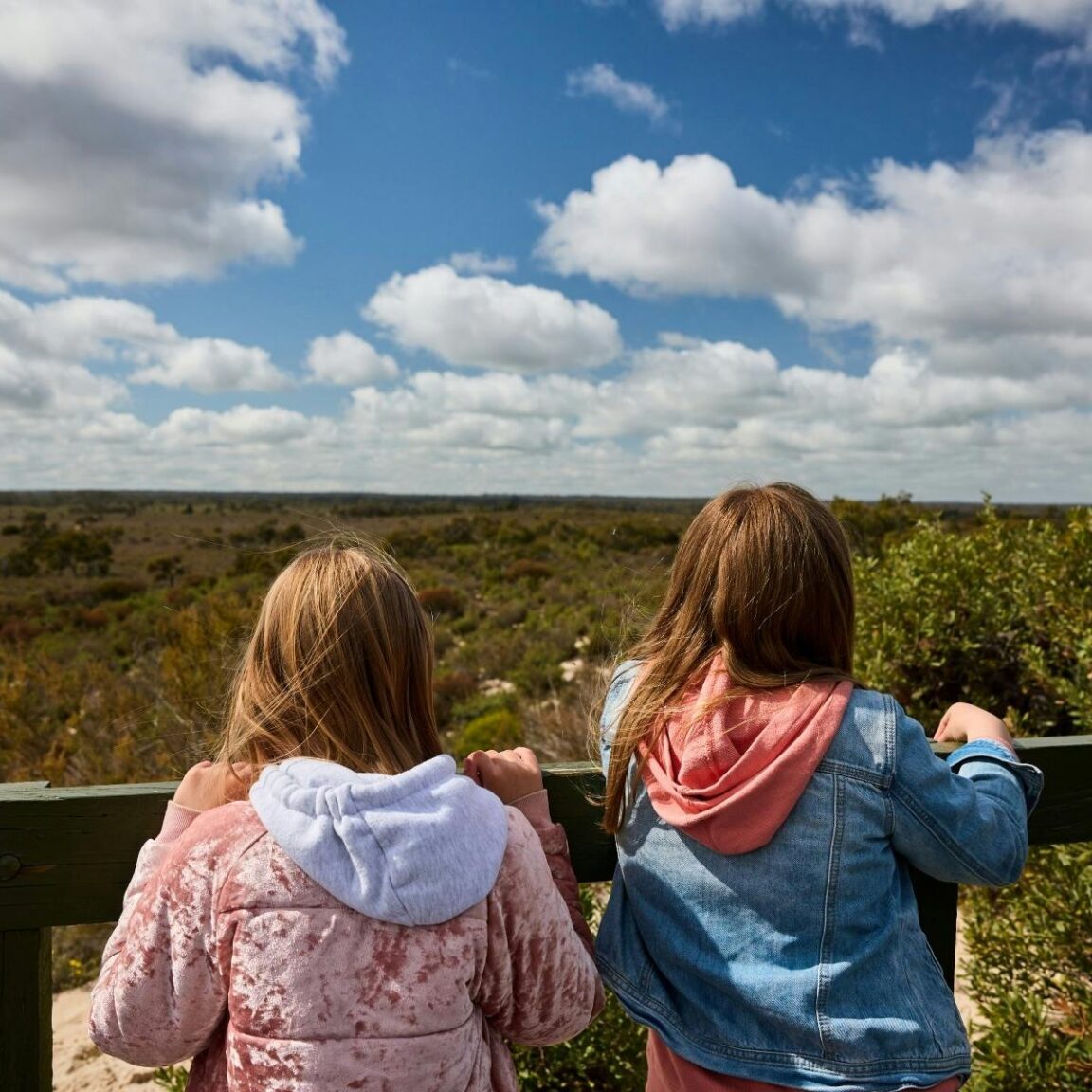 Two girls looking out over a lookout fence across scrubby desert landscape