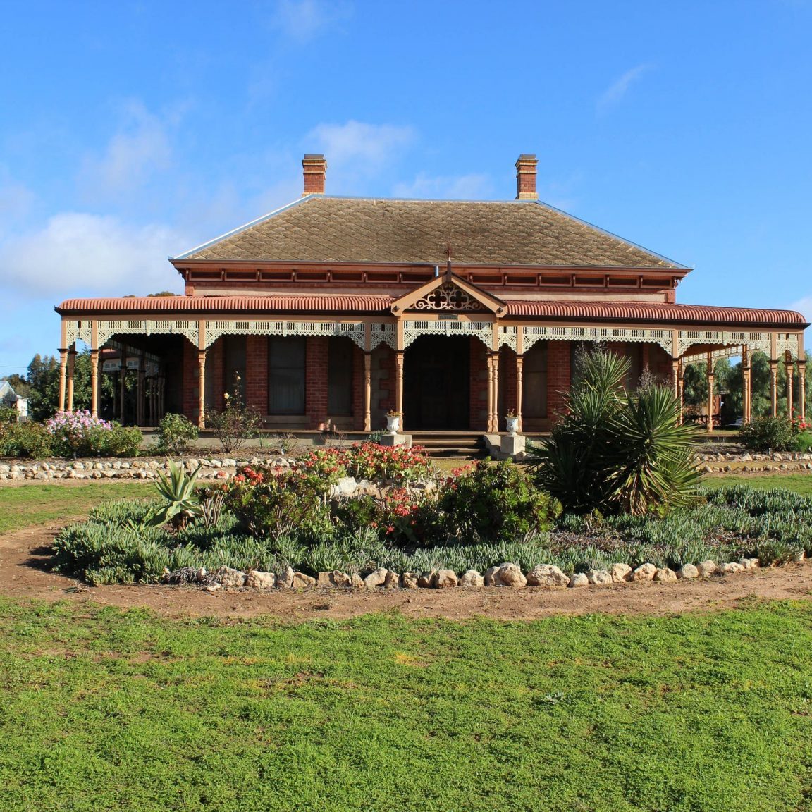 Front entrance and veranda of Georgian style heritage homestead with lawn and garden in foreground