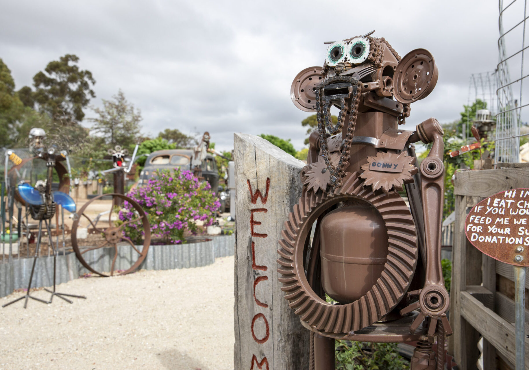 A large metal sculpture holding a welcome sign in front of an open garden area.