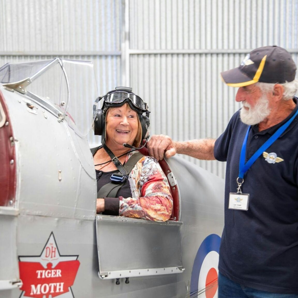 Woman sitting in an old airplane with a flying cap talking to a man standing beside the plane