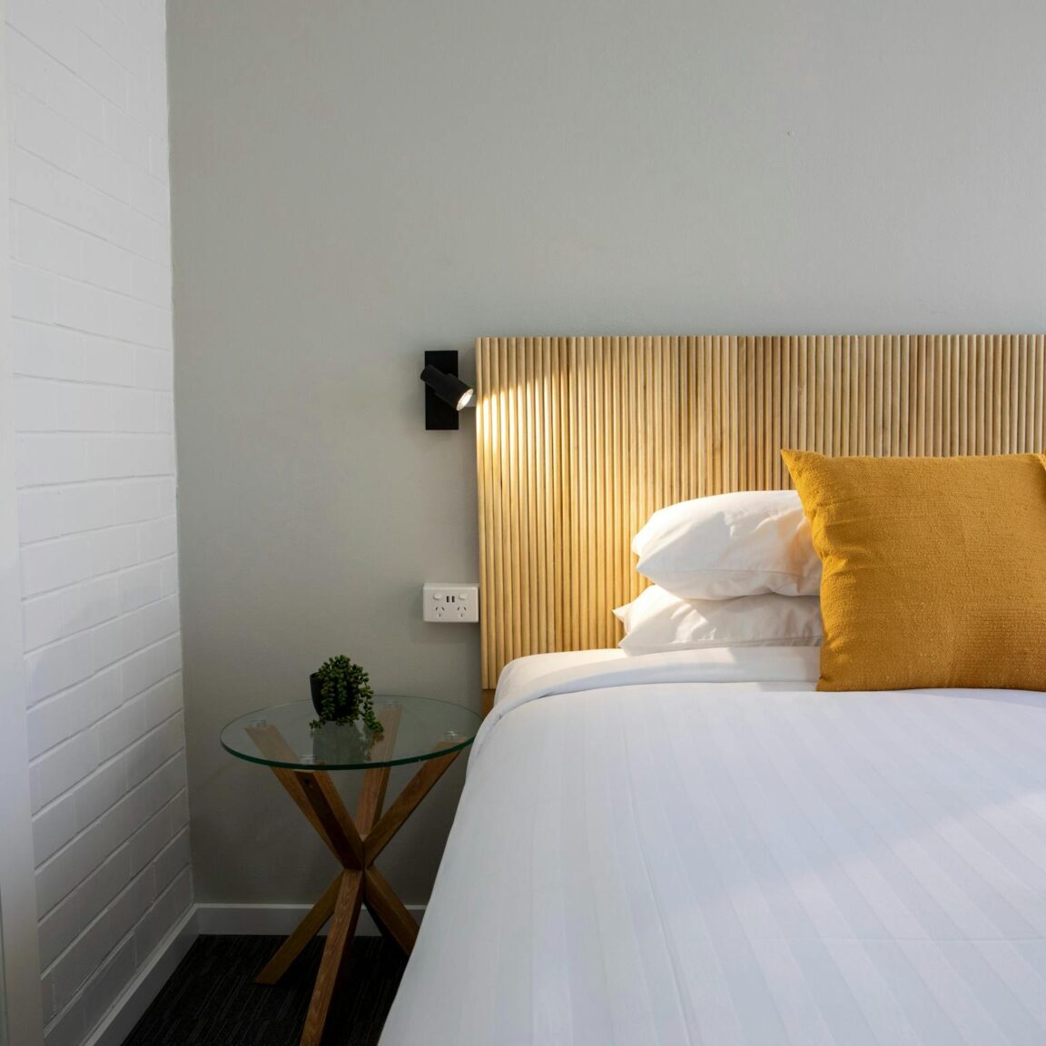 Image of a pillow on a bed in a motel style room with a reading lamp on the wall
