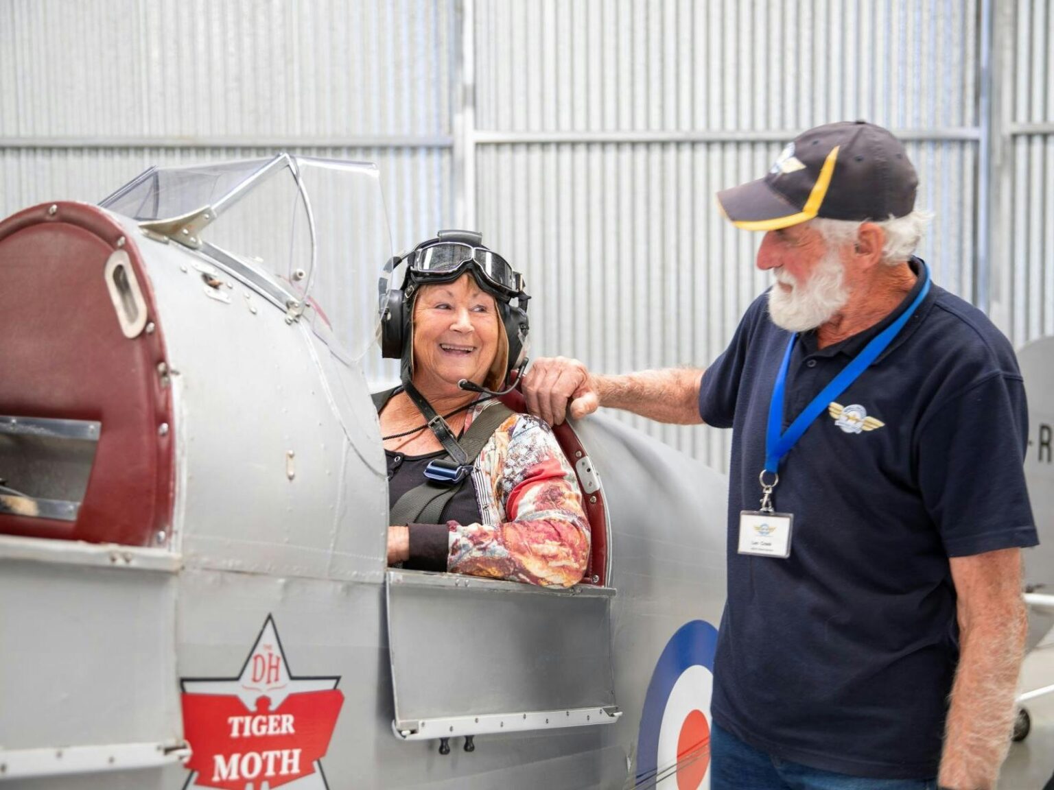 Woman sitting in an old airplane with a flying cap talking to a man standing beside the plane