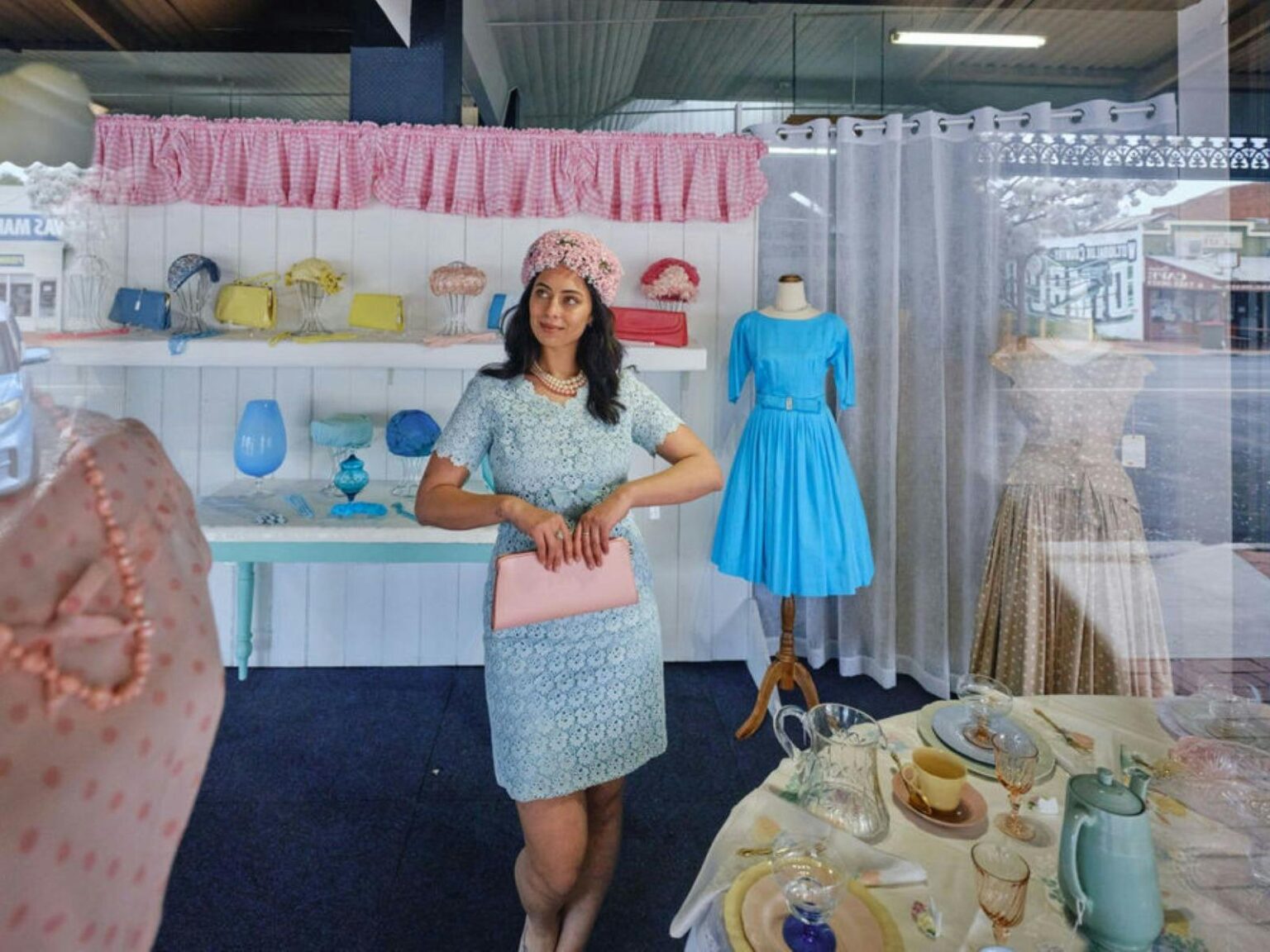 Young person standing in a window display dressed in vintage clothing