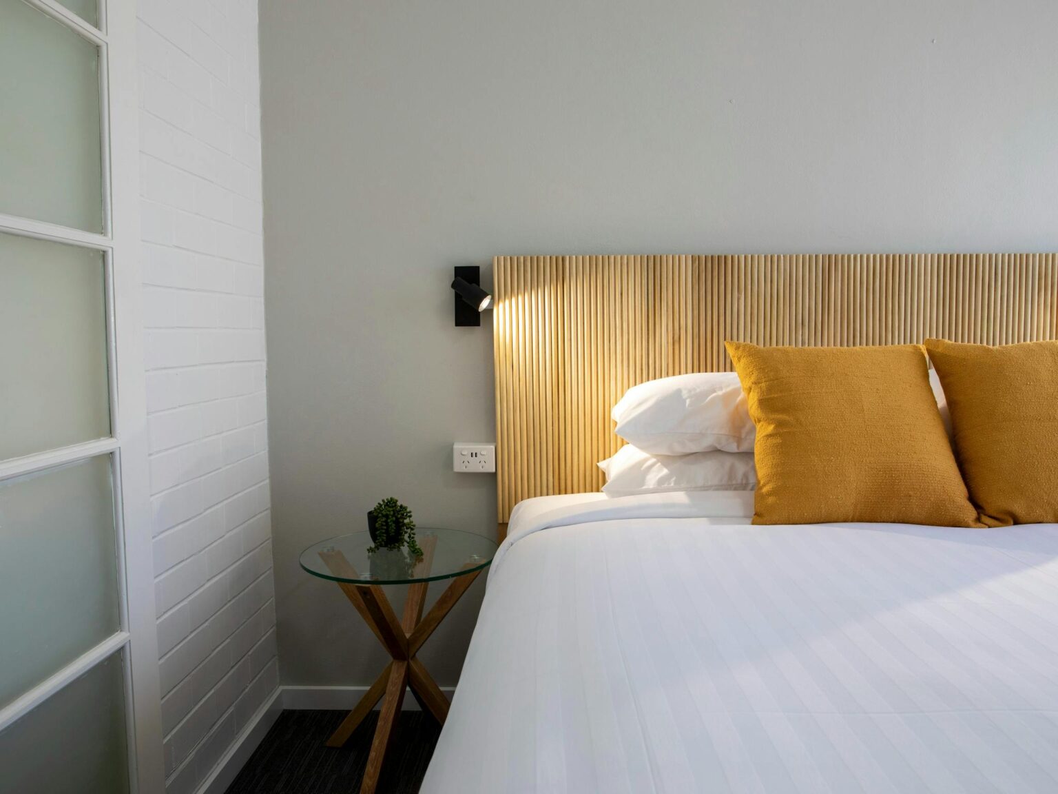 Image of a pillow on a bed in a motel style room with a reading lamp on the wall